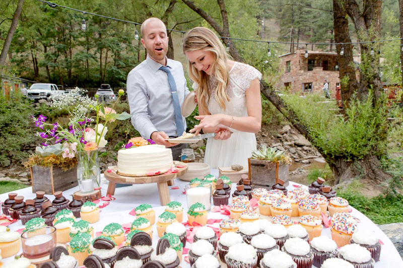 Couple cutting wedding cake at outdoor reception dessert table at A-Lodge Boulder Colorado destination wedding venue